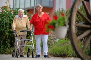 Eine Altenpflegerin geht mit einer Bewohnerin am Rollator spazieren.