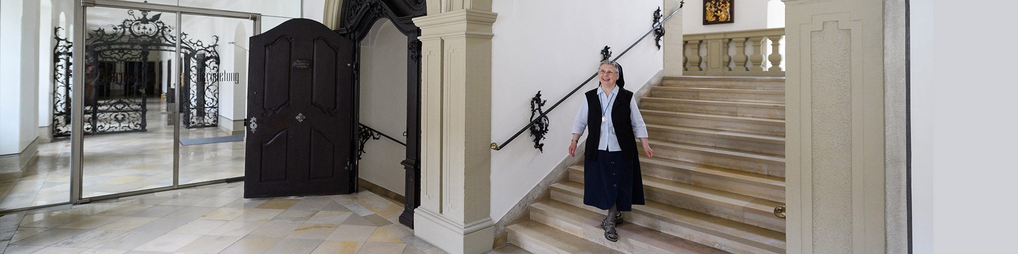 Eine Oberzeller Schwester läuft lächelnd eine Steintreppe herunter. Diese befindet sich im Mutterhaus, ein barockes Gebäude.