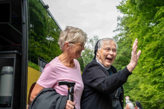 Eine Schwester winkt vom Lift, sie wird von einer Frau gestützt.