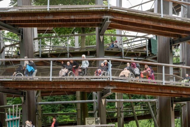 Mehrere Seniorinnen werden im Rollstuhl auf dem Holzsteg geschoben.