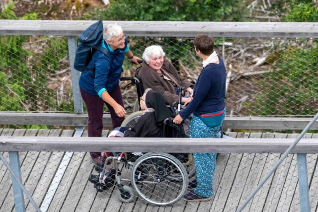 Begegnung auf dem Holzsteg: zwei Seniorinnen im Rollstuhl und ihre Begleiterinnen.