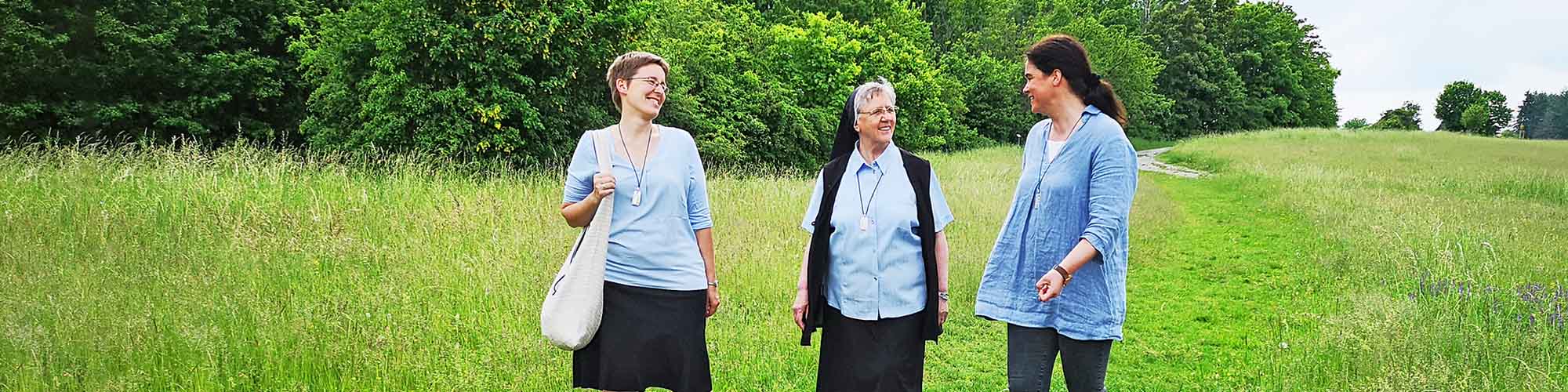 Drei Oberzeller Franziskanerinnen laufen auf einer Wiese im Wasserschutzgebiet oberhalb des Kloster Oberzell gelegen und unterhalten sich.
