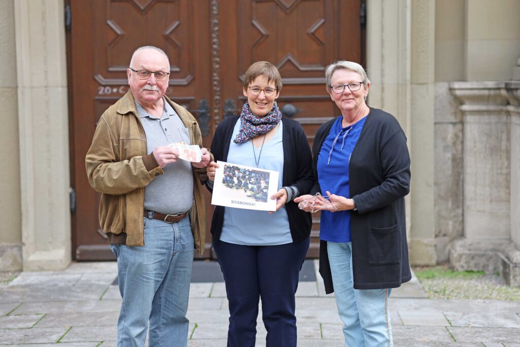 Günter Führich und Monika Ziller vom Obst- und Gartenbauverein Zell stehen vor der Klosterkirche in Oberzell und überreichen Sr. Juliana Seelmann eine Spende für den Kindergarten Antonia-Werr in Südafrika.