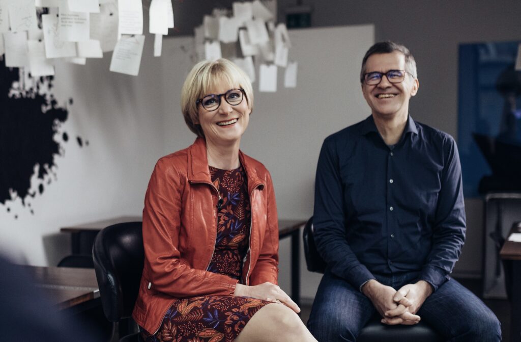 Eine Frau und ein Mann sitzen und lächeln in die Kamera.