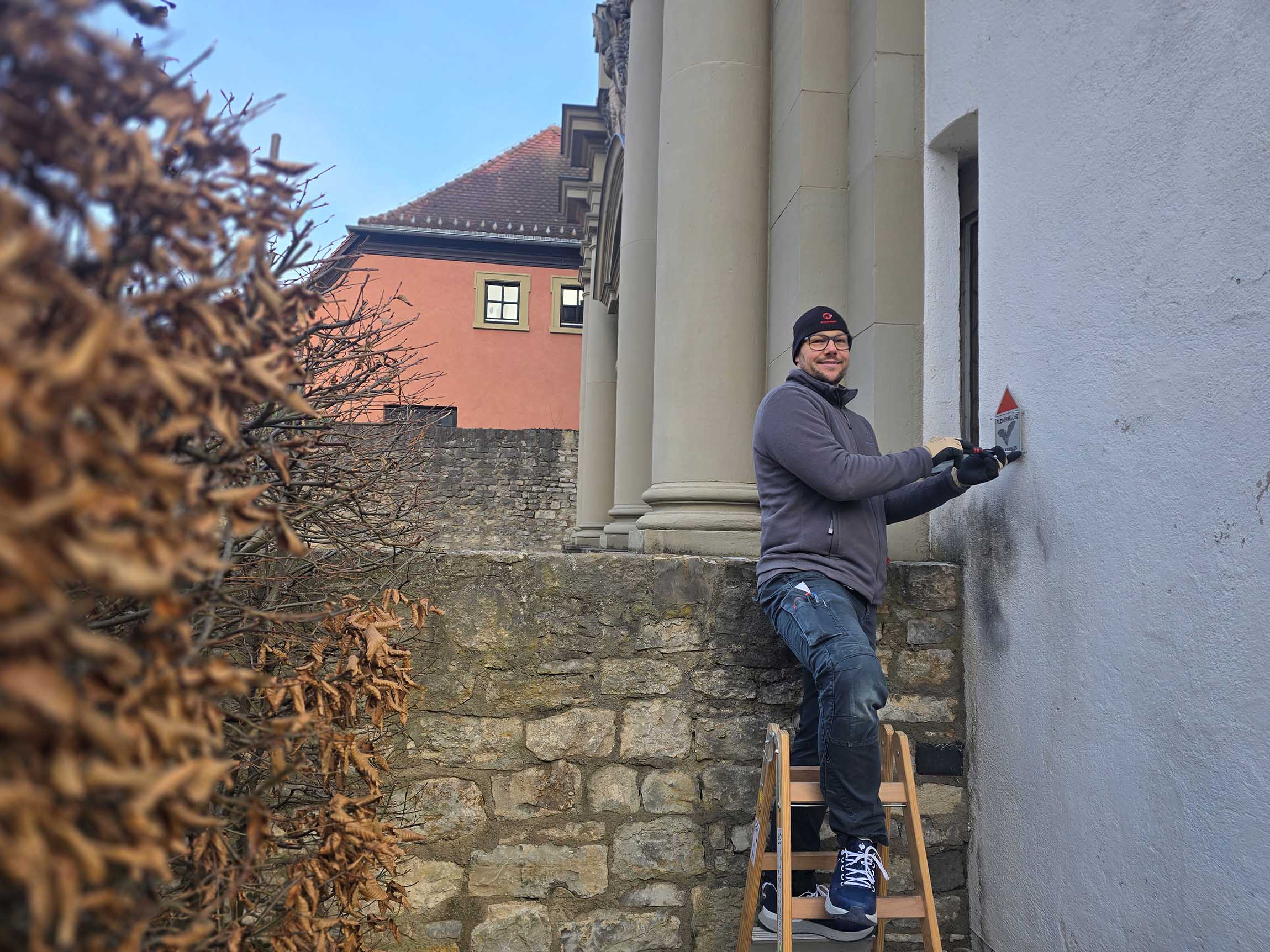 Alexander Gittel, Vorarbeiter der Handwerker, schraubt die Fledermausplakette an die Kirche